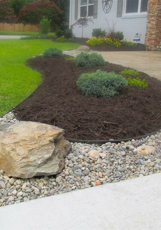 Landscaping installed in front of a home with river rock, mulch, and plants.